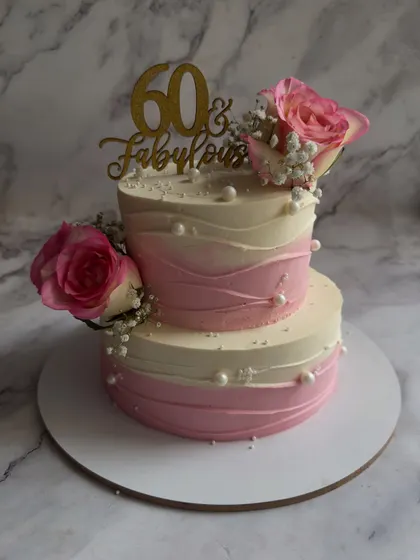 Celebrating "60 & Fabulous" with a two-tier design. This cake features a soft pink ombre effect, delicate sugar pearls, and is crowned with fresh roses and baby's breath.