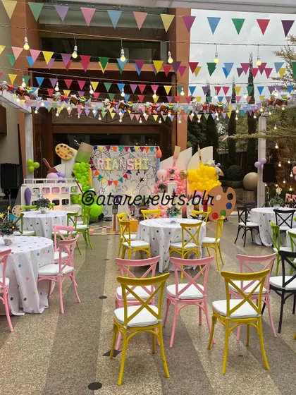 A wide view of an art-themed birthday party. The venue is filled with colorful chairs, polka-dotted tablecloths, and art-inspired decorations, creating a bright and creative space.