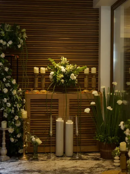 A beautifully styled console table combining modern and rustic elements. The setup features white and green floral arrangements, candles, and a wooden cabinet, creating a sophisticated welcome area.