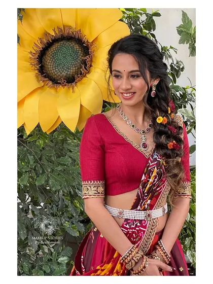 A close up of Prathima's haldi look. The makeup is fresh and youthful, with a beautiful braided hairstyle decorated with colorful flowers for a fun, festive touch.