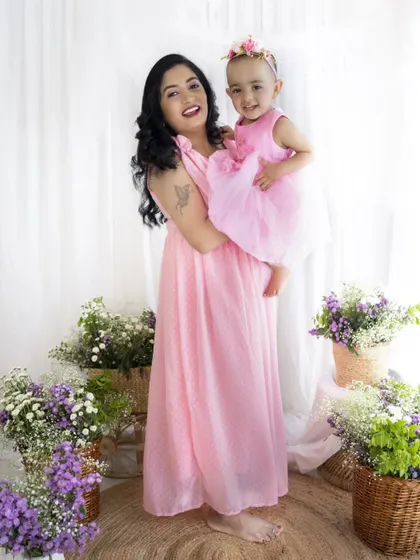 A full-length portrait of a mother holding her daughter, showcasing their beautiful matching dresses and the floral studio setup.