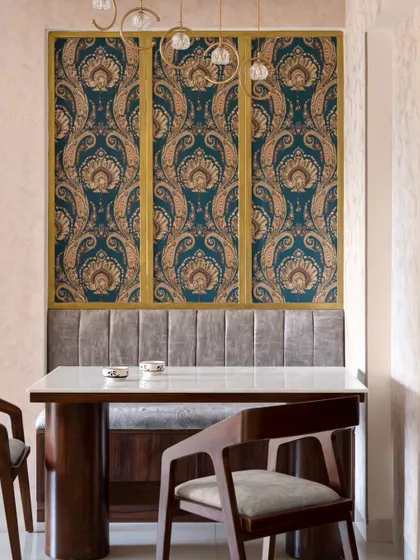 A detail of the custom dining nook in 'Muditā', with its plush upholstered bench and a backdrop of rich damask wallpaper framed in gold.