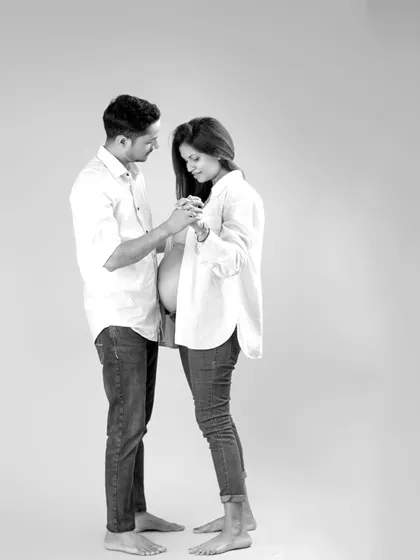 This black and white portrait captures a candid, gentle interaction between the expecting parents. Dressed in simple, coordinating outfits, their connection and the beautiful silhouette of the baby bump are the focus.