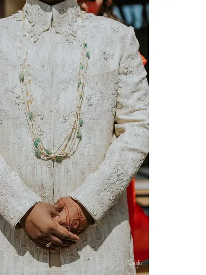 A close-up of the groom's wedding day sherwani. The intricate embroidery and the layered pearl and emerald necklace create a look of regal elegance.