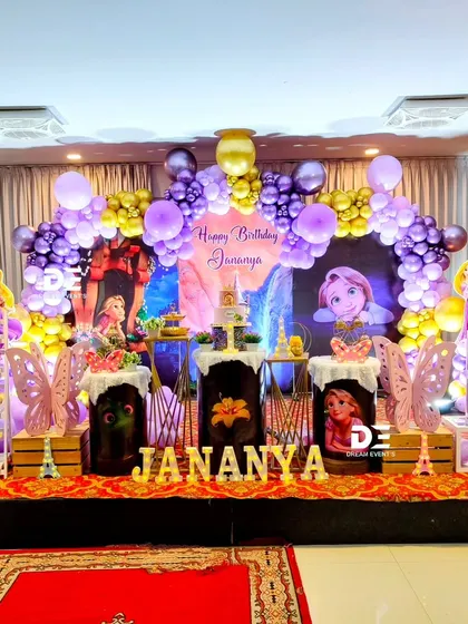 A royal Rapunzel-themed party for Jananya's first birthday. The decor is filled with shades of purple and gold, featuring character cutouts and butterfly accents for a magical touch.