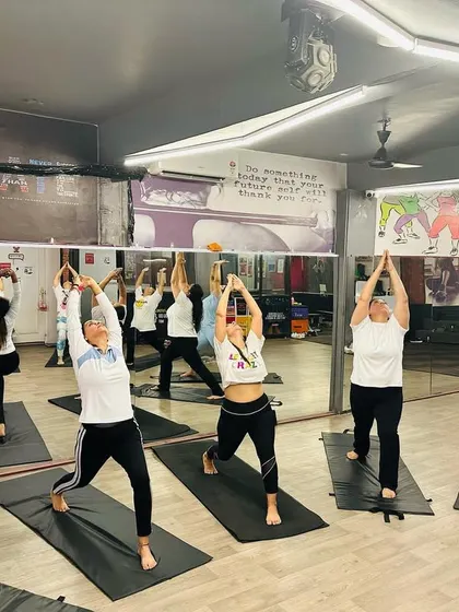 The studio filled with the calm, focused energy of a warrior pose sequence. You can see the reflection in the mirror, showing a full class moving as one.
