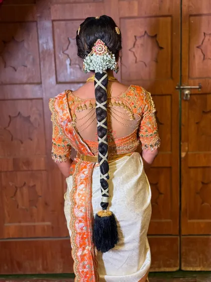 A full back view of the bride's hairstyle and her intricately designed blouse. The criss-cross braid and floral accessory create a harmonious and elegant look.
