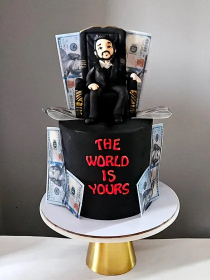 This bold, all-black fondant cake was designed with the theme "The World Is Yours." It features a detailed, hand-sculpted figurine on a throne, surrounded by edible money prints for a powerful and striking look.