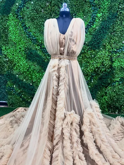 This beige designer gown features beautiful ruffles and a flowing train. It's a unique and elegant option available for rent from my collection.