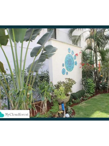 This garden corner is full of life, featuring large Bird of Paradise plants and a decorative wall mandala. The design uses layers of different plants to create depth and visual interest.