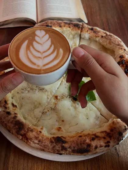 Holding a cup of our expertly made coffee over a Pizza Bianca. The perfect pairing.