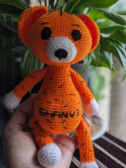 This personalized tiger toy, 'Shanvi', is held up against a leafy green plant.