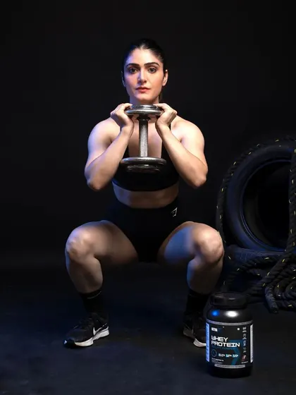An action shot demonstrating a lifestyle application of the product. The female model is mid-squat, associating the supplement with strength and performance. The product is placed clearly in the foreground, ensuring it remains the focus even during a dynamic scene.