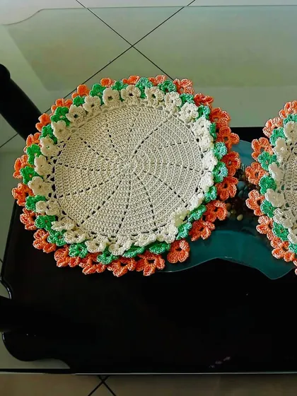A bright and cheerful floral placemat with layers of orange, green, and cream petals. This piece is sure to brighten up any space.