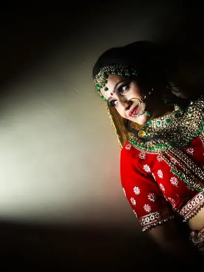 A beautifully composed portrait using a single light source to create a dramatic effect. This technique highlights the bride's profile and the rich color of her red lehenga against the dark background.