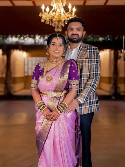 The happy couple posing at the entrance. The bride's soft glam makeup and elegant hairstyle look stunning with her purple Kanjeevaram saree, creating a picture-perfect moment.