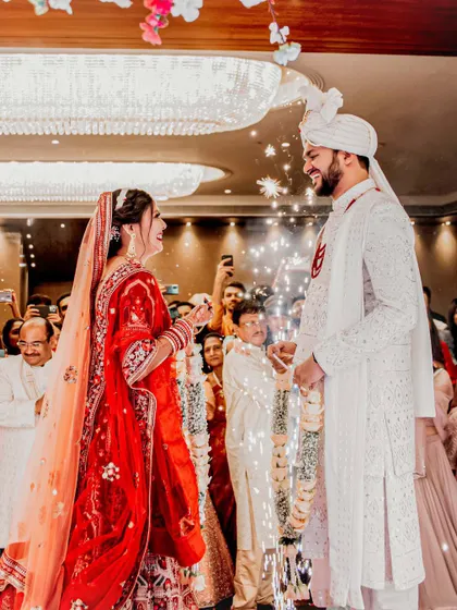 The Varmala exchange is a moment of playful excitement and acceptance. Here, the bride garlands the groom amidst a shower of sparklers, with their families cheering them on. It's a perfect capture of joy during a Hindu wedding.
