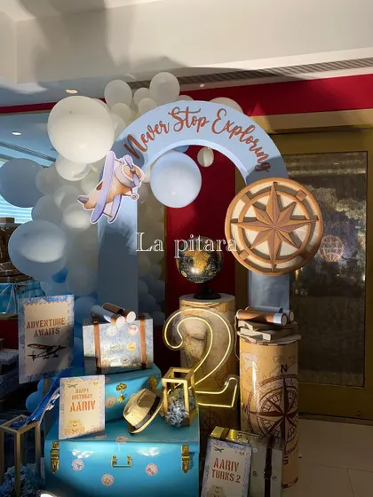 A welcome display for a travel-themed second birthday, with vintage suitcases, a compass rose, and a sign that says 'Never Stop Exploring'.