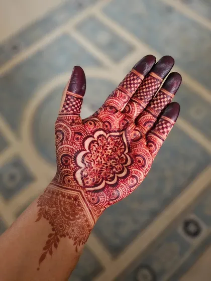 This photo captures the rich, reddish-maroon tone of a fully developed henna stain. The central mandala and finger details are incredibly dark and striking.