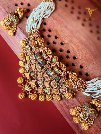 This gold choker combines intricate gold detailing, regal meenakari hues of red and green, and delicate pearl strings to create an accessory that feels as grand as the stories it carries.