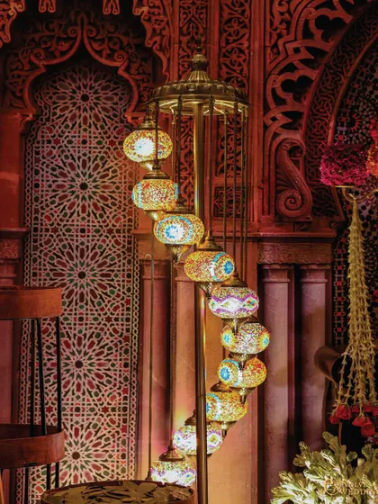 A tall, spiraling Turkish mosaic lamp stands as a beautiful decorative element. Its intricate, colorful glasswork adds an authentic touch to the Indo-Islamic theme.