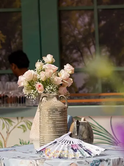 A simple arrangement of pink roses in a rustic vase, seen through a foreground of purple flowers. This shot captures the soft, dreamy quality of the event's floral design.
