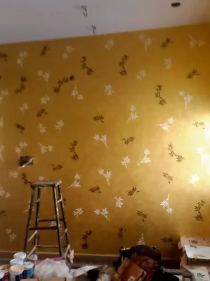 A golden-yellow wall featuring a scattered floral stencil pattern in white and brown, shown mid-project to highlight the application process.
