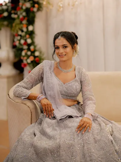A graceful portrait of the bride, Anusha, seated on a couch at her reception, looking elegant in her grey lehenga.