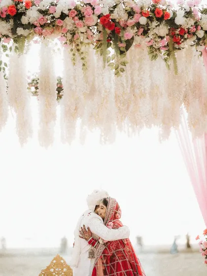 A warm embrace under the floral mandap. This shot shows how the makeup looks beautiful and natural in a bright, outdoor setting.