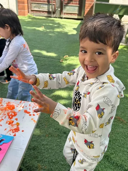An ecstatic smile says it all. This little star is having the time of his life during our outdoor Holi celebration, filled with color, music, and laughter.