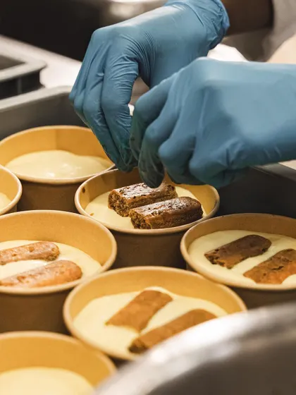 A chef carefully places coffee-soaked ladyfingers into the cups for our Tiramisu. Each layer is built with precision.