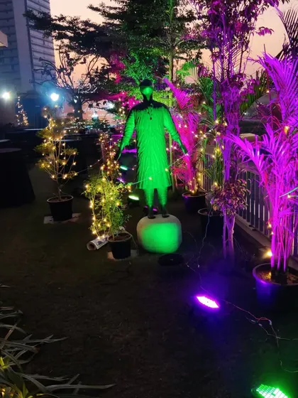 A detail shot of the garden decor, where even statues and plants are incorporated into the lighting scheme. A statue is highlighted with green light, integrating it into the overall festive and artistic theme of the evening.