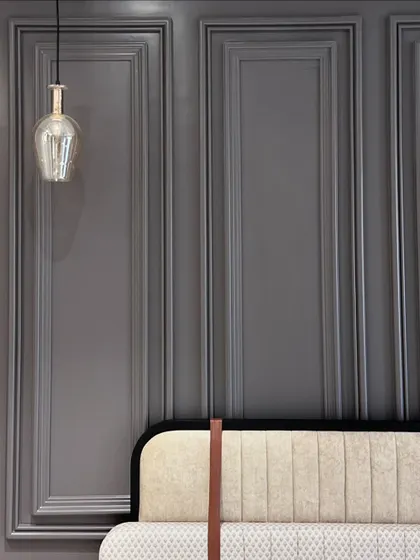 A detail shot of a custom headboard against a grey paneled wall. The design features a unique leather strap detail, adding a subtle, sophisticated touch.