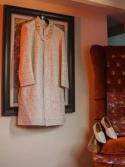 The groom's wedding attire, a stunning white sherwani, is elegantly displayed before the ceremony. This shot, along with his shoes, captures the anticipation of him getting ready.