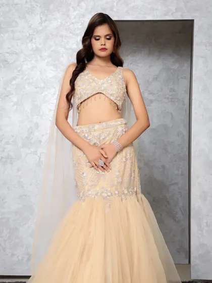 A professional shot of a model in a beige mermaid-style lehenga-gown with a delicate cape. This silhouette is perfect for a cocktail or engagement party.