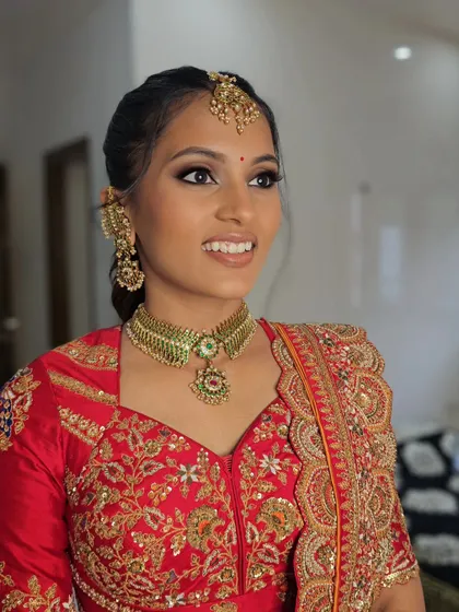 A close-up portrait of Nishra, looking stunning in her red and gold embroidered outfit.