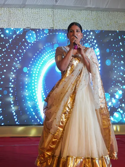 Dressed in a beautiful white and gold ensemble, holding the mic and ready to kick off a night of celebration.