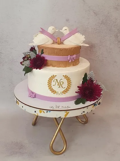This two-tiered cake is topped with two lovely fondant doves, symbolizing love and commitment. The custom monogram and delicate purple ribbons make it perfect for an engagement or Roka ceremony.