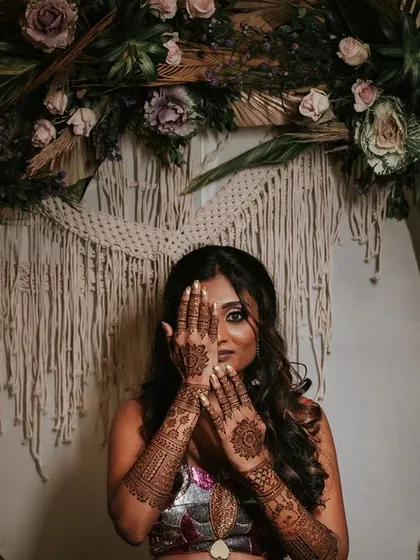 A bride with intricate henna designs on her hands, framed by a rustic floral arch. This image showcases the blend of traditional artistry with modern, bohemian decor.