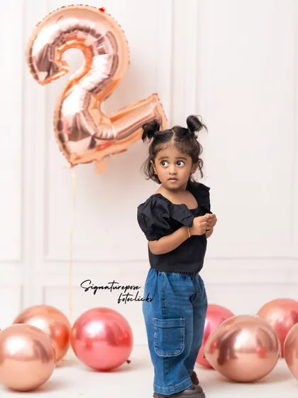 A stylish portrait for a second birthday. This image shows a different pose from the same session, capturing her standing confidently amidst the rose-gold balloons.