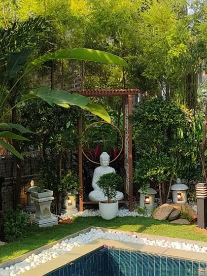 This poolside Zen garden creates a dedicated space for peace and meditation. A serene white Buddha statue is framed by a wooden arch and surrounded by bamboo, Japanese-style lanterns, and carefully selected rocks, embodying tranquility and mindful design.