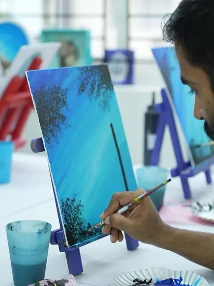 A close-up of a participant painting a night sky on canvas. The dabbing technique is used to create the effect of distant trees.