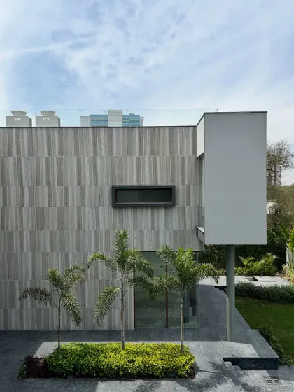 The facade of the Rosewood residence showcases a composition of textured stone, clean white planes, and carefully placed greenery. Small palm trees in a dedicated planter add a touch of organic life to the structured architectural forms.