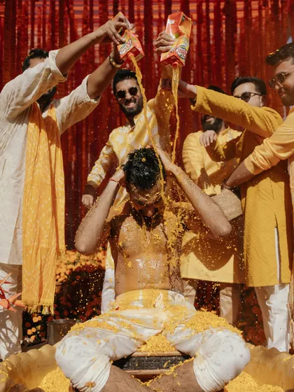 A fun and unrestrained moment from a Haldi ceremony, where the groom is playfully doused by his friends.