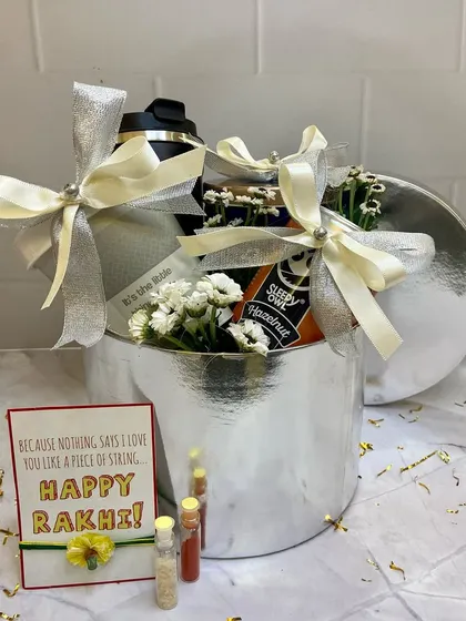 A sleek and modern Rakhi hamper in a silver box. This gift set includes a shaker bottle and coffee, perfect for a fitness-loving brother, complete with a 'Happy Rakhi' card and traditional elements.