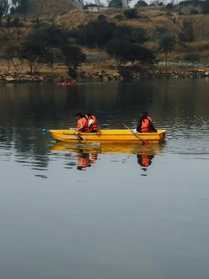 A team paddles together in a yellow boat on the calm lake, with the reflection of the sky on the water.