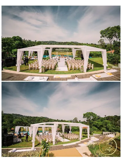 An aerial and wide view of the outdoor wedding venue, showing the entire tented mandap setup in a beautiful natural setting.