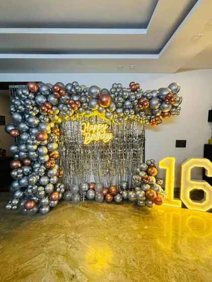 A stylish and modern 16th birthday party backdrop. This design uses a trendy silver sequin wall, a neon 'Happy Birthday' sign, and a balloon frame in metallic silver and rose gold, complemented by large light-up marquee numbers.