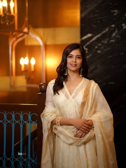 This shot, set against a grand staircase, adds a touch of architectural elegance to the portrait. The warm lighting complements the off-white ethnic wear perfectly.