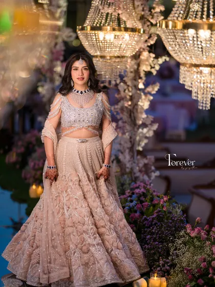 A full-length portrait of the bride against a backdrop of magnificent chandeliers and floral arrangements. The lighting is carefully designed to make her and her stunning lehenga sparkle.